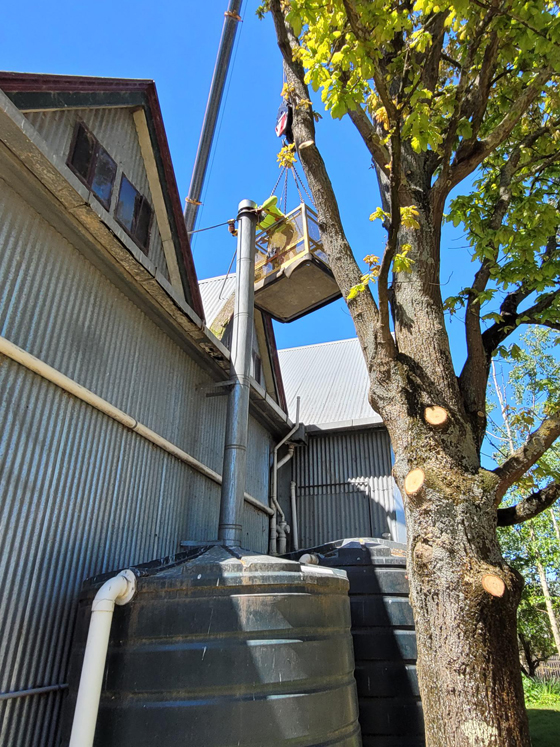 close side view of crane with basket and arm extended over two story tin shed winery with worker repairing cowl