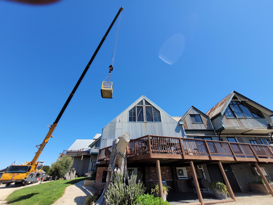 far side view of crane with basket and arm extended over two story tin shed winery