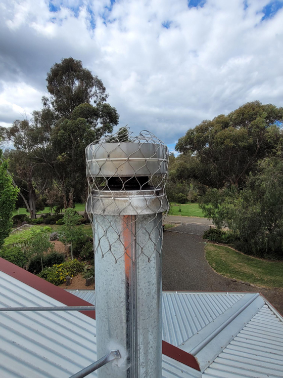 after side closeup view of new flue and cowl on a tin roof with bird netting installed