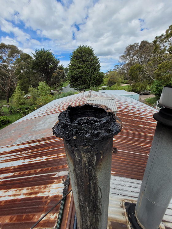 before close up side view dirty flue and damaged broken cowl on tin roof alongside another repaired flue in good condition