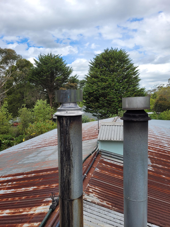 after side view of repaired flue and stainless steel cowl on tin roof alongside another repaired flue in good condition