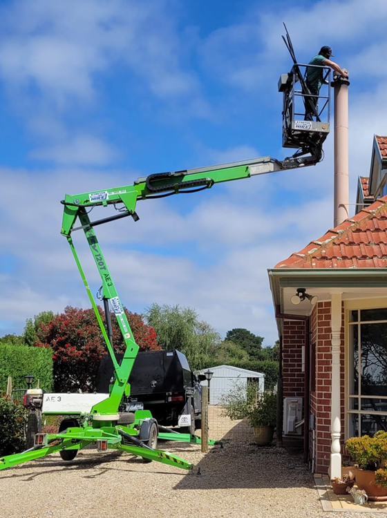 green cherry picker with worker repairing and cleaning repairing flue 3 metres above roof height