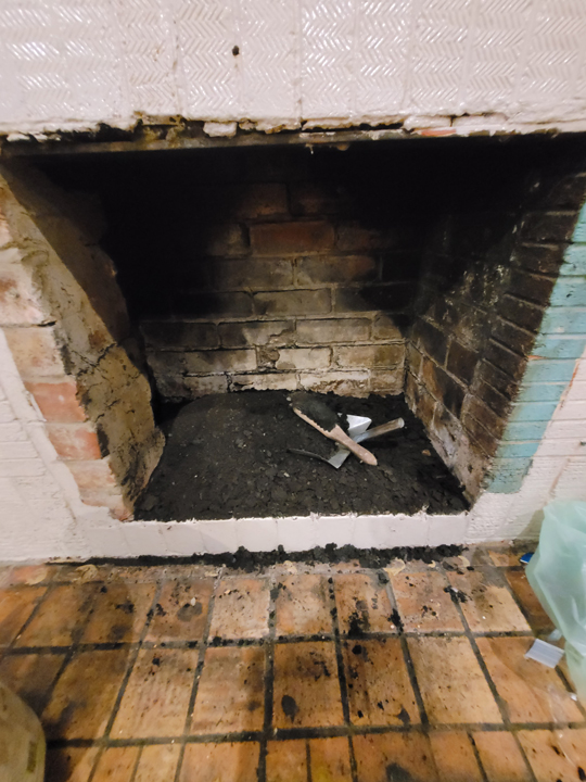 before image front view of very dirty brick fireplace filled with ash underneath dustpan and broom